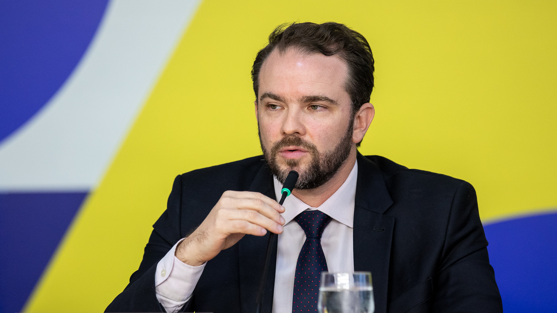 Ministro da Fazenda, Dario Durigan, fala ao microfone em um debate sobre a taxa das blusinhas e o impacto no comércio nacional.