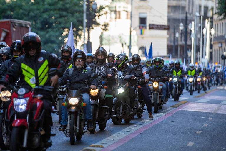 Grande grupo de entregadores pilotando motocicletas em uma avenida urbana, representando o público-alvo de programas como o financiamento de moto pelo governo.