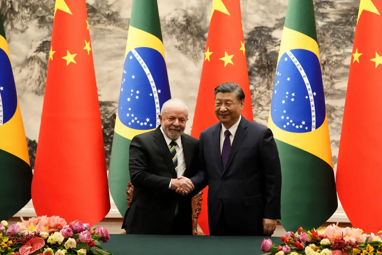O presidente Lula e o líder chinês Xi Jinping apertam as mãos em meio a bandeiras do Brasil e da China, simbolizando acordos bilaterais e comerciais.