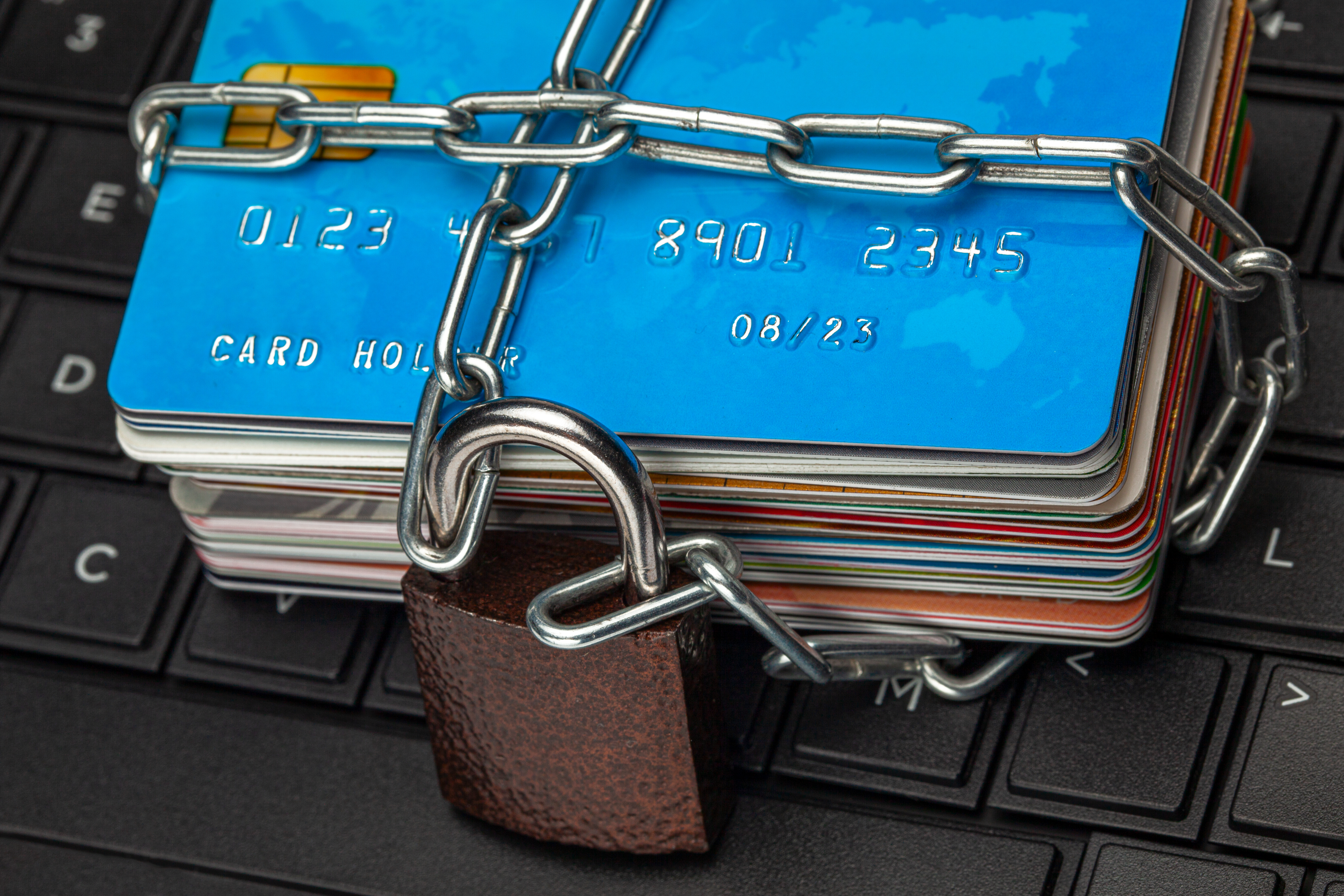 Pilha de cartões de crédito e recursos financeiros amarrados com corrente e cadeado sobre um teclado de computador, ilustrando a tributação e segurança de ativos.