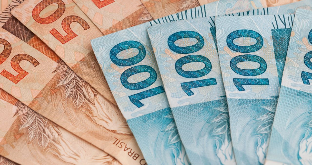 Notas de reais dispostas em leque, representando a arrecadação de impostos e o impacto da dívida pública federal nas finanças corporativas.