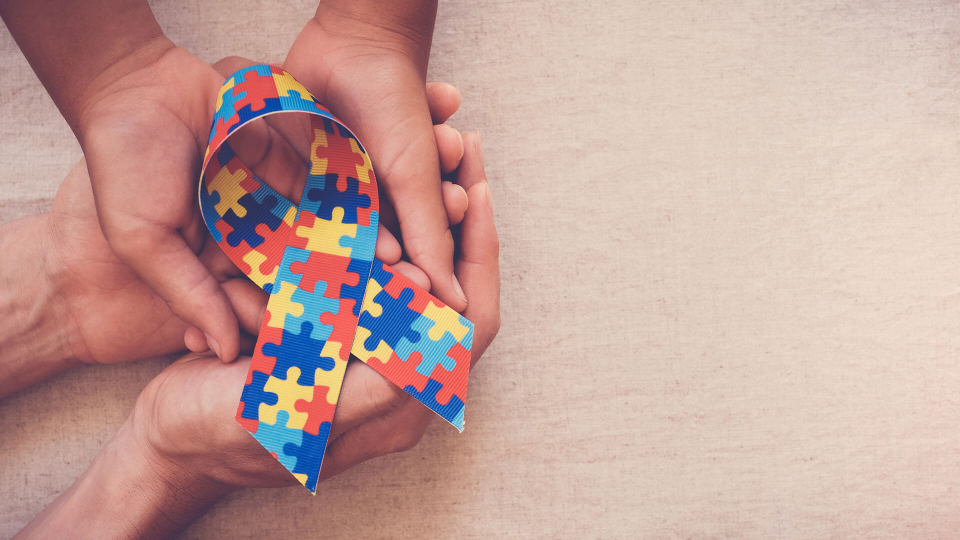 Mãos unidas seguram a fita colorida de conscientização do autismo, simbolizando direitos como a isenção de IPVA e ICMS para PcD.
