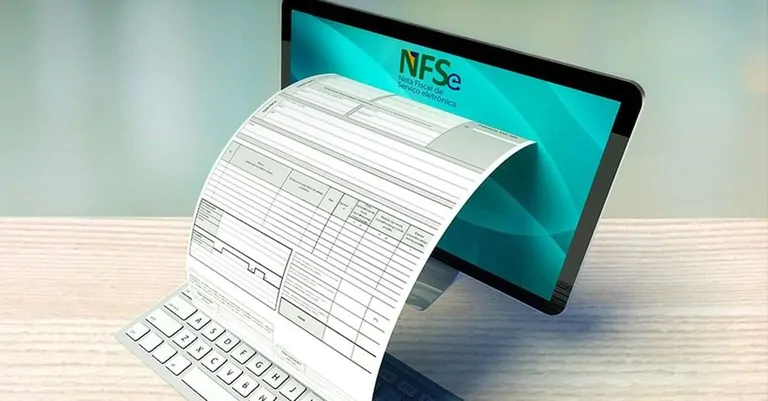 Monitor de computador exibindo a logo da NFS-e, com um documento fiscal impresso saindo da tela sobre um teclado, ilustrando as mudanças no cClassTrib com a Reforma Tributária.