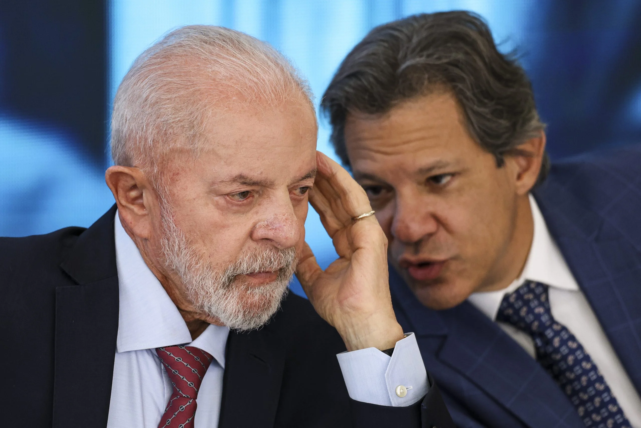 O presidente Lula aparece pensativo enquanto o ministro Fernando Haddad conversa com ele, ilustrando o cenário de preocupação com o rombo histórico nas estatais federais.