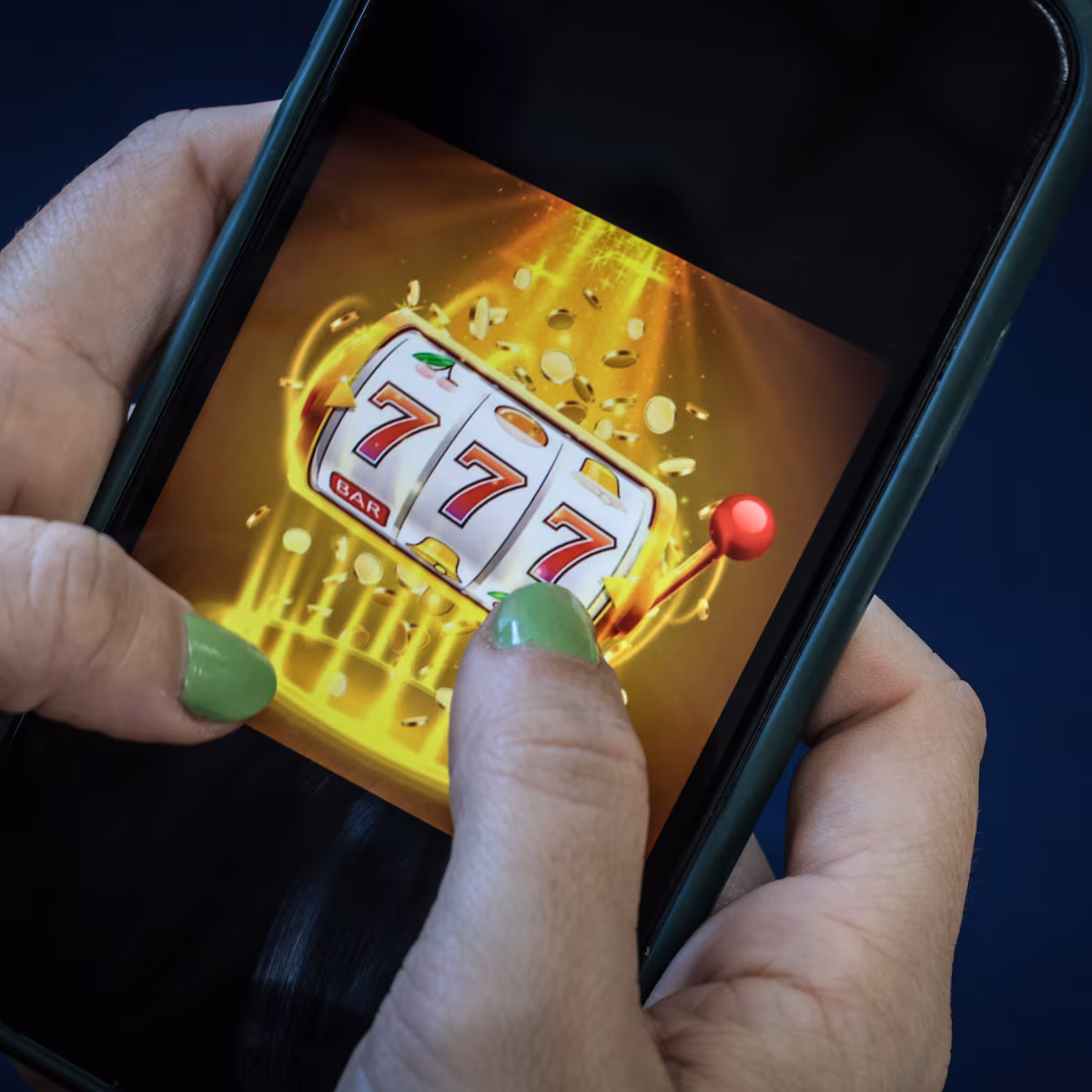 Mãos seguram um smartphone exibindo um jogo de caça-níqueis online, representando o impacto financeiro das apostas em bets.