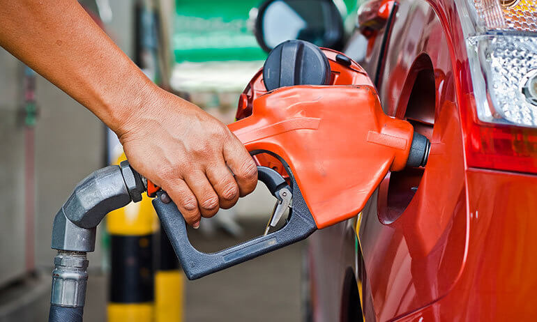Mão segurando bico de bomba de combustível para abastecer um carro vermelho em um posto, ilustrando os custos que compõem a margem de lucro na nota fiscal de combustível.