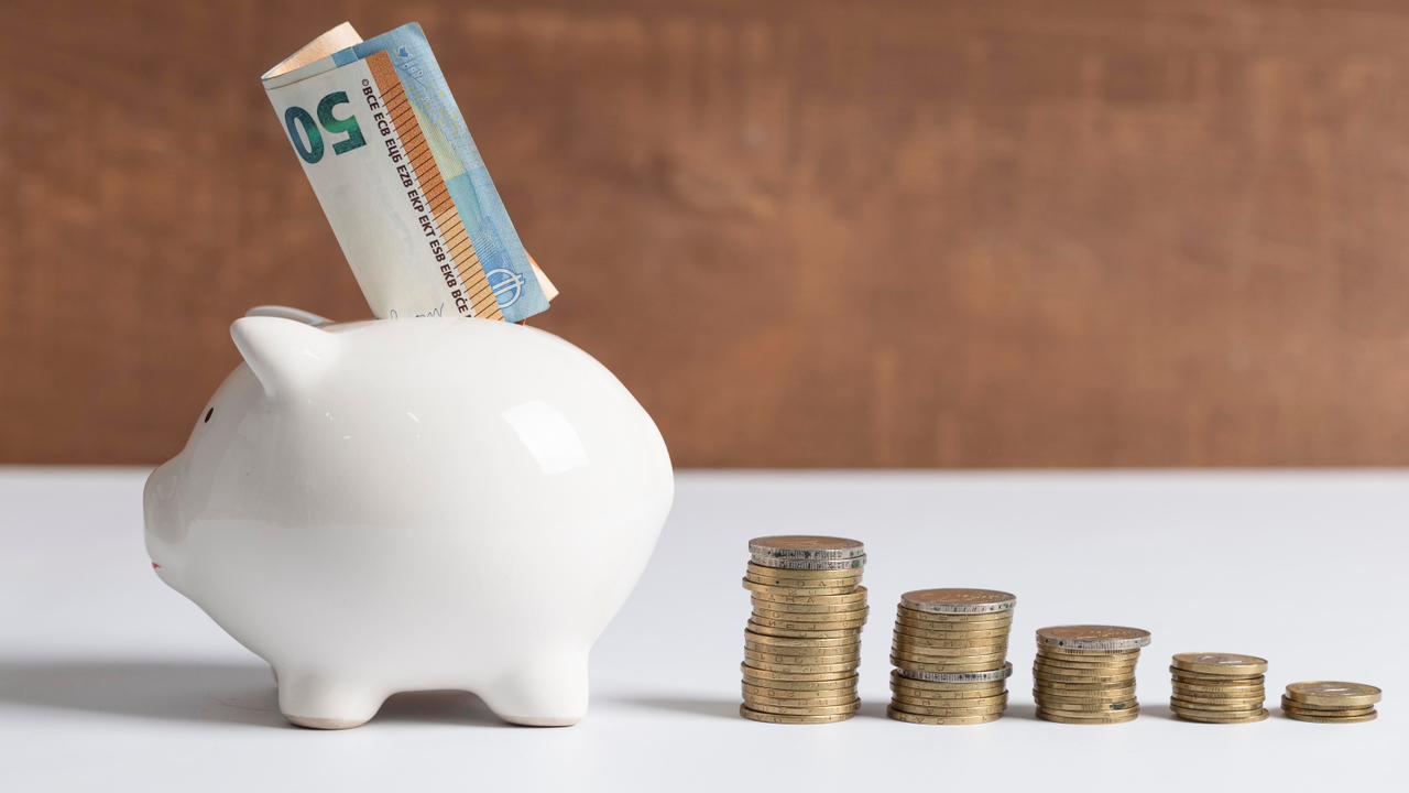 Cofrinho branco em formato de porquinho com notas e pilhas de moedas ao lado, ilustrando o controle financeiro que o Split Payment no Pix traz para o caixa da empresa.