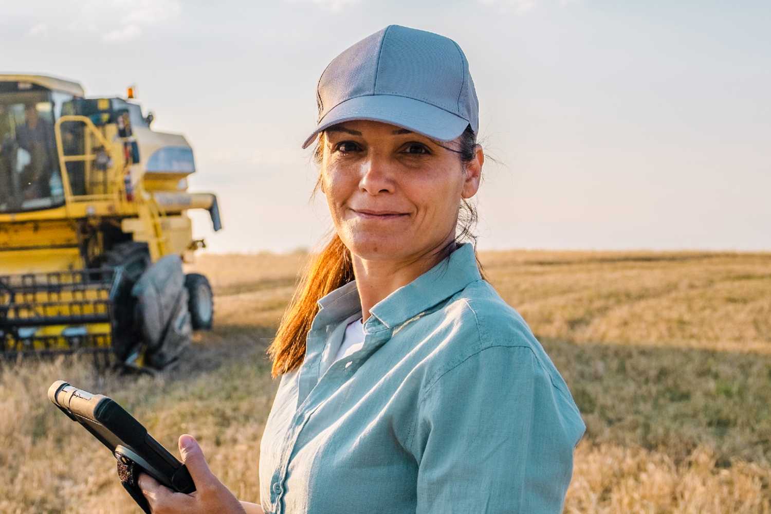 Produtora rural sorrindo em uma plantação com um tablet na mão, representando a profissionalização da gestão e a recuperação judicial no agro.