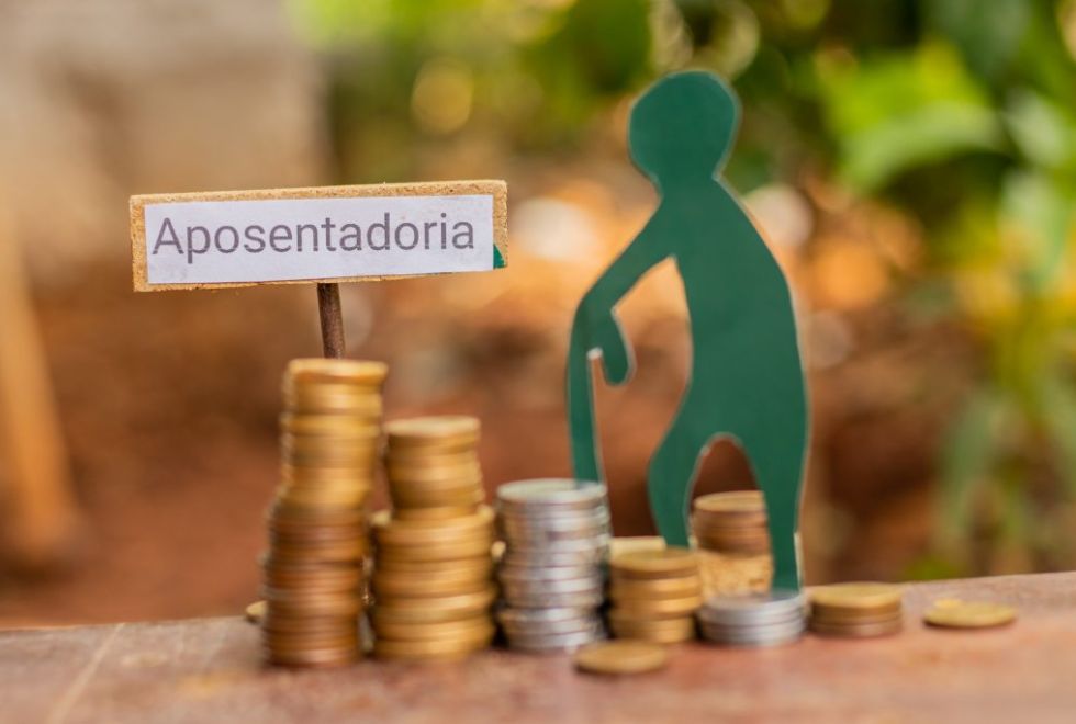 Boneco verde curvado apoiado em uma bengala ao lado de pilhas de moedas e uma placa com a palavra Aposentadoria, ilustrando a dúvida se a aposentadoria do MEI vai mudar.
