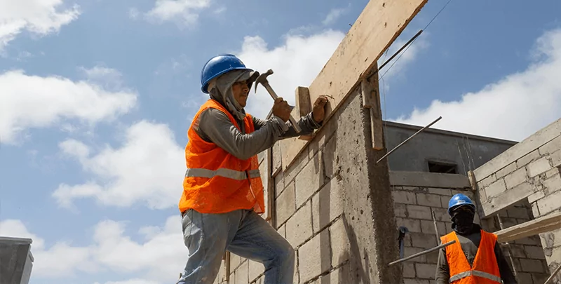 Dois operários com capacetes e coletes de segurança trabalham em uma obra afetada pelos impactos da reforma tributária na construção civil.