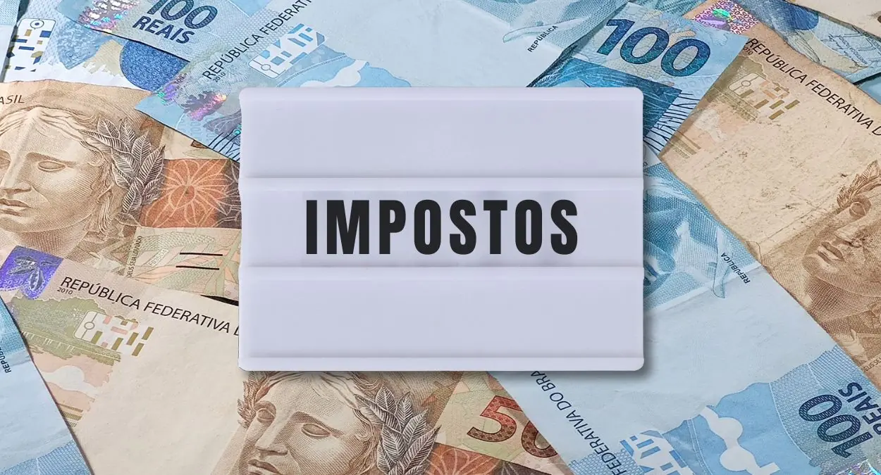 Placa luminosa branca com a palavra IMPOSTOS sobreposta a notas de dinheiro brasileiras, ilustrando o contexto da Reforma Tributária e a escolha do Simples Híbrido em 2026.