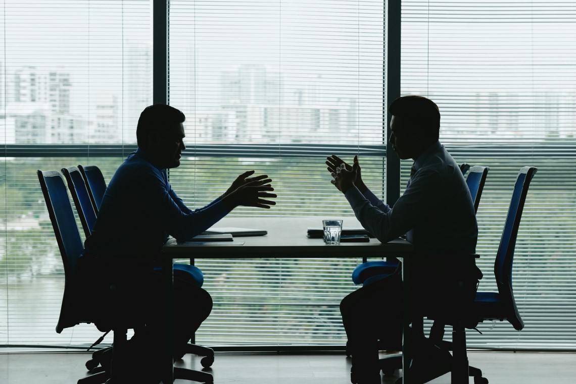 Silhuetas de dois executivos reunidos em uma sala de reunião corporativa para discutir a recuperação judicial e dívidas empresariais.