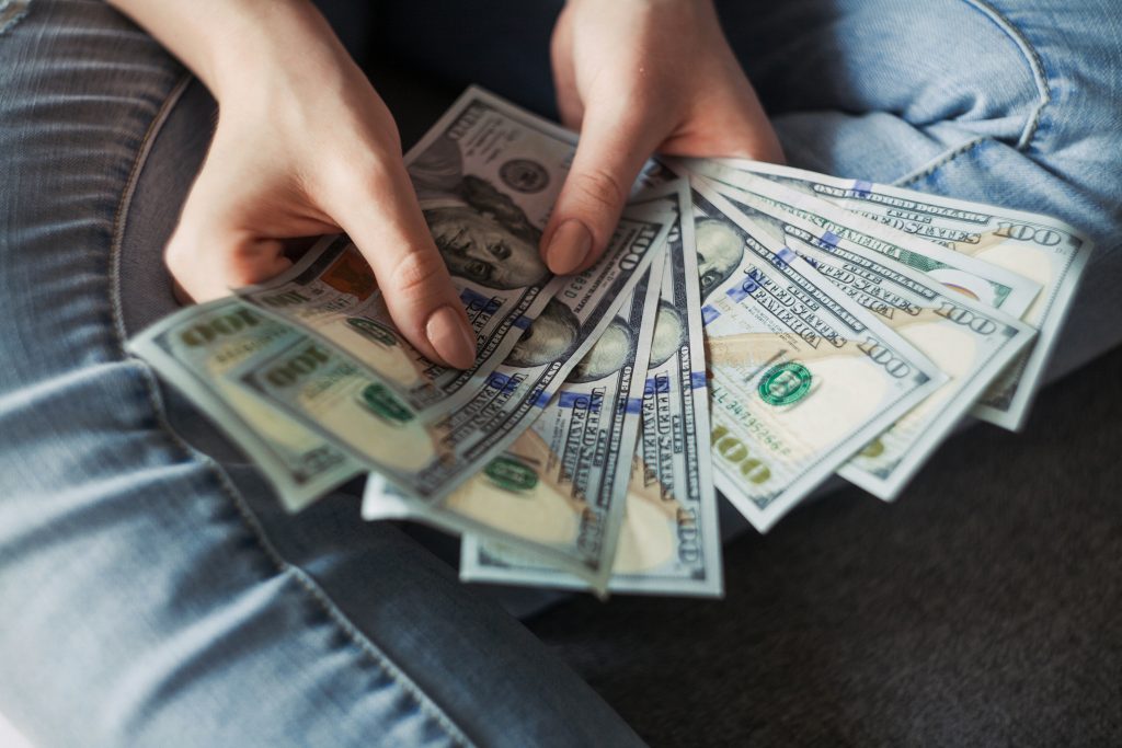Pessoa sentada segurando notas de dinheiro nas mãos, ilustrando o impacto financeiro e o planejamento de caixa da empresa.