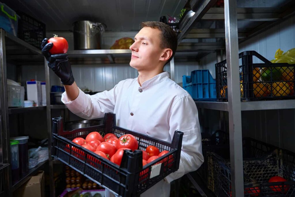 Chef de cozinha analisando um tomate em estoque, representando o impacto dos custos e da Reforma Tributária em bares e restaurantes.