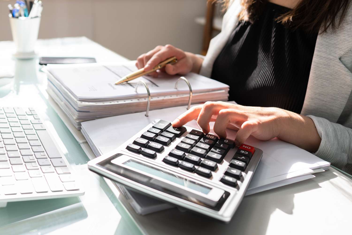 Contadora calcula impostos e revisa documentos financeiros em sua mesa de trabalho, destacando a importância do profissional diante da Reforma Tributária.