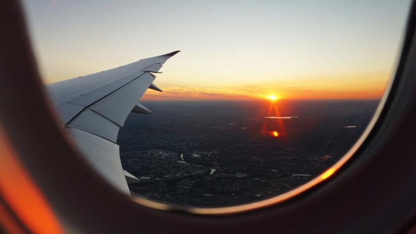 Vista da asa de um avião e do pôr do sol pela janela, ilustrando a partida do país para quem vai regularizar a situação fiscal.