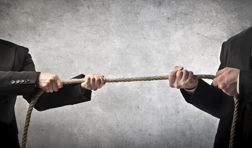 Duas pessoas de terno puxando uma corda em lados opostos, representando um litígio empresarial que pode ser resolvido por arbitragem tributária.