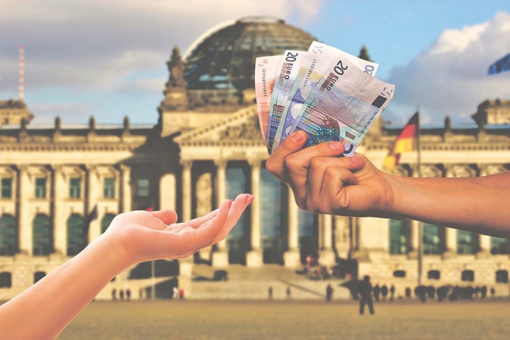 Mãos segurando notas de dinheiro em frente a um grande edifício público, ilustrando a recuperação de créditos tributários como a exclusão do ISS da base de PIS e COFINS.