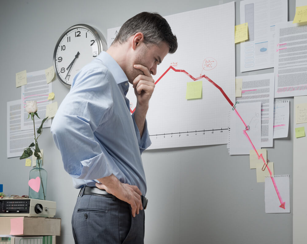 Homem pensativo observa um gráfico financeiro com queda acentuada, ilustrando cenários de crise e recuperação judicial corporativa.