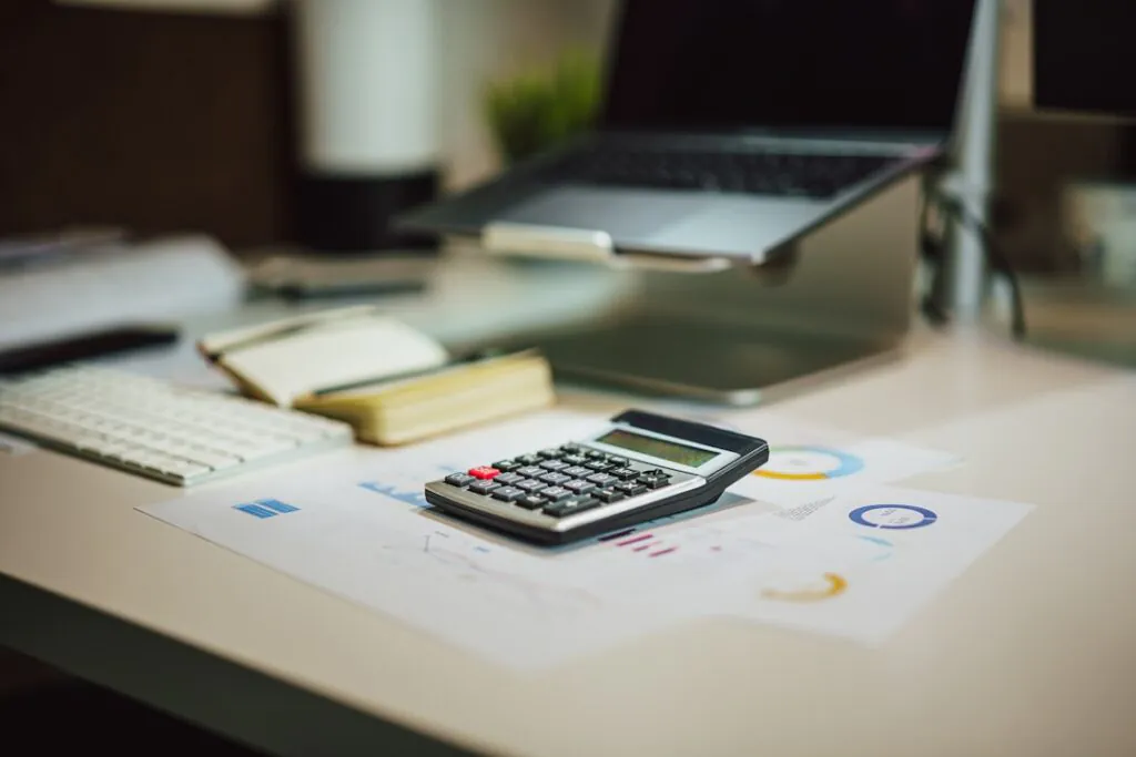 Mesa de escritório com calculadora sobre gráficos financeiros, ilustrando o planejamento por trás do faturamento bilionário no varejo.