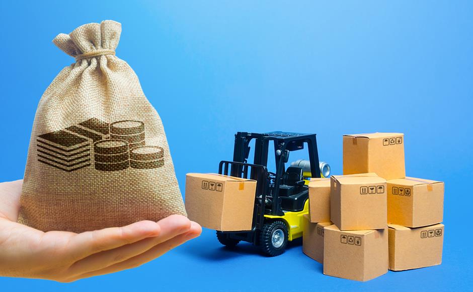 Mão segurando um saco de dinheiro em miniatura ao lado de uma empilhadeira e caixas de papelão, representando os impactos fiscais de incentivos de ICMS no IRPJ e CSLL.