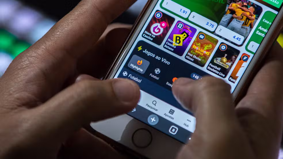 Pessoa segura smartphone exibindo aplicativo de apostas esportivas, ilustrando o tema bets na mira da Receita.