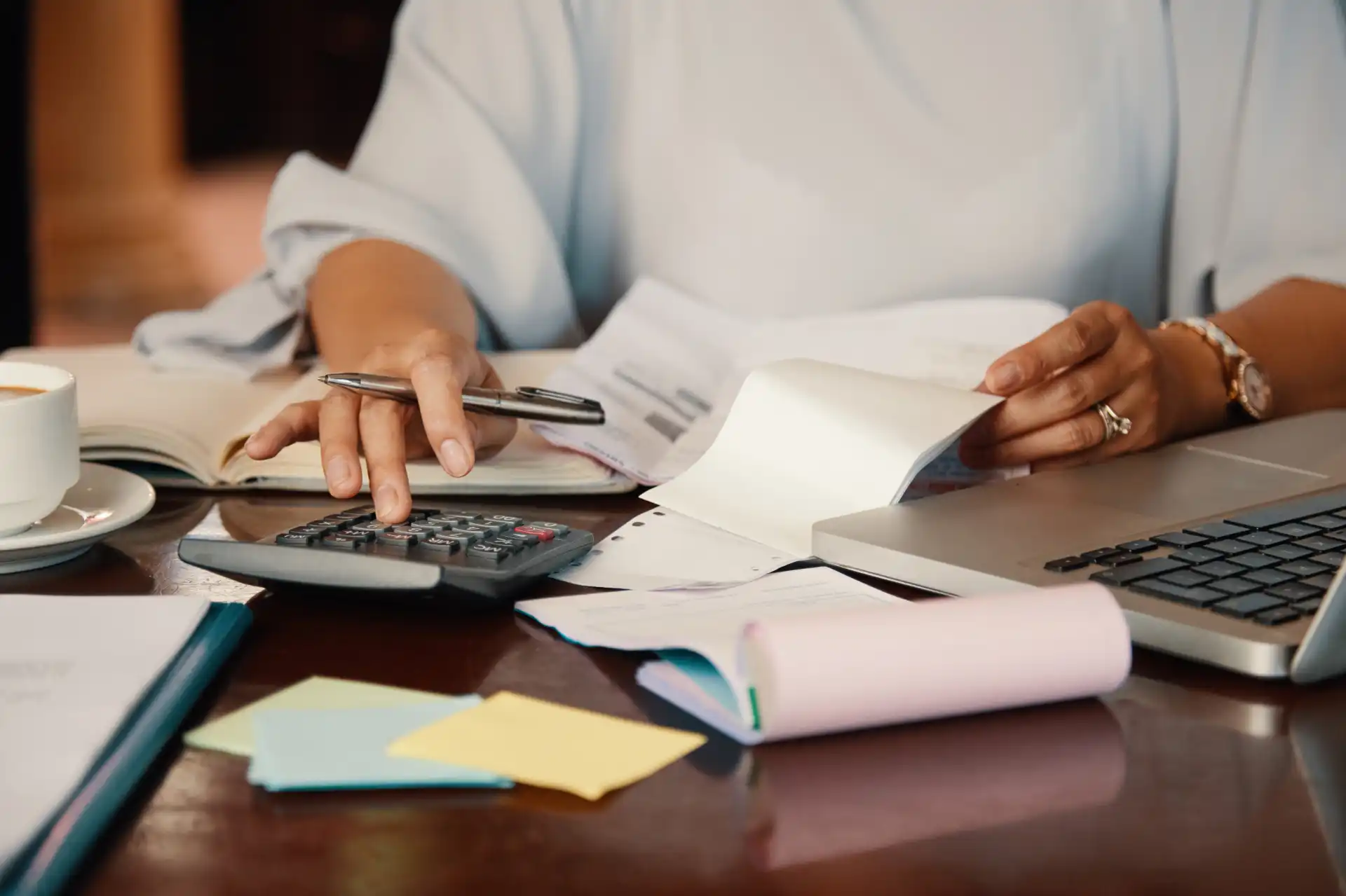 Mulher usa calculadora e analisa documentos financeiros na mesa, ilustrando o planejamento para o Orçamento 2027 do seu negócio.