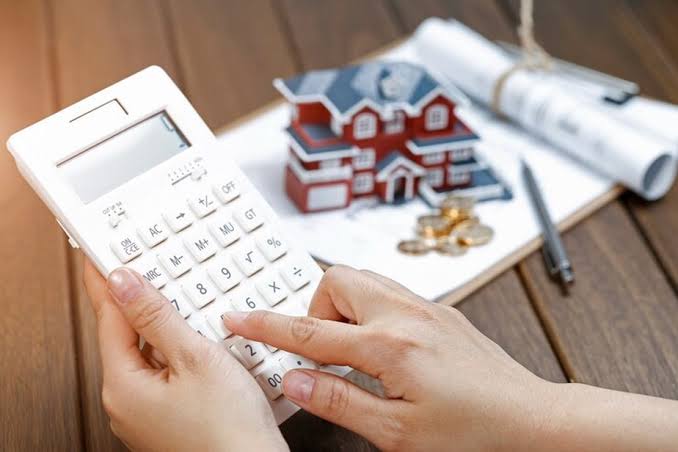 Mãos usando uma calculadora ao lado de uma maquete de casa e moedas, ilustrando o impacto financeiro de que o imposto da herança vai aumentar.