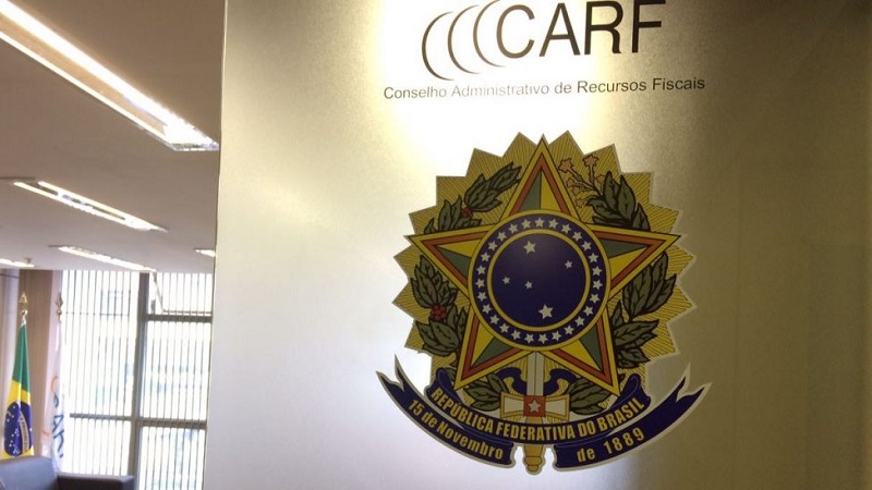 Placa na parede com o logotipo e o nome do CARF, Conselho Administrativo de Recursos Fiscais, e o brasão da República Federativa do Brasil, ilustrando discussões sobre retroatividade benigna e redução de passivos fiscais.