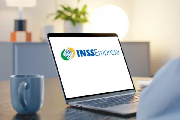 Notebook aberto sobre uma mesa de madeira exibindo a logo do INSS Empresa na tela, ilustrando como funciona o sistema para empregadores.