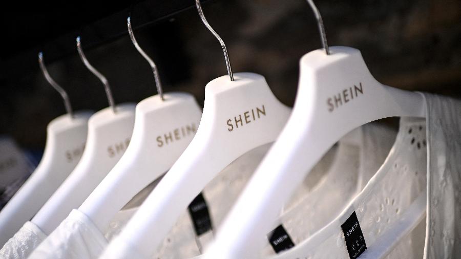 Cabides brancos com a marca Shein pendurados em uma arara, ilustrando compras de roupas afetadas pela taxa das blusinhas.