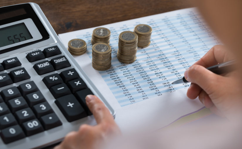 Calculadora, pilhas de moedas e planilhas sobre a mesa ilustram a preparação das empresas para a IFRS 20.