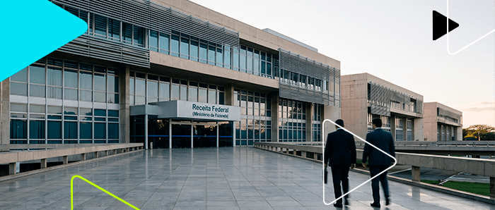 Dois homens de terno caminham em direção ao prédio da Receita Federal, ilustrando a discussão sobre conformidade tributária, correção de erros fiscais e prevenção de fiscalizações.