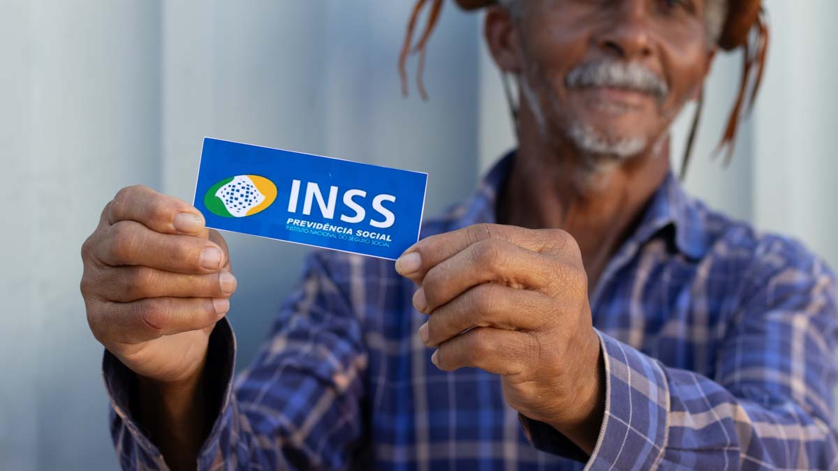 Homem sorridente segura um cartão com a logo do INSS, ilustrando os direitos dos segurados durante o período de graça.