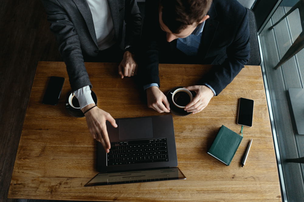 Dois profissionais sentados à mesa de madeira analisando dados financeiros em um notebook, ilustrando a necessidade de separar finanças pessoais e corporativas.