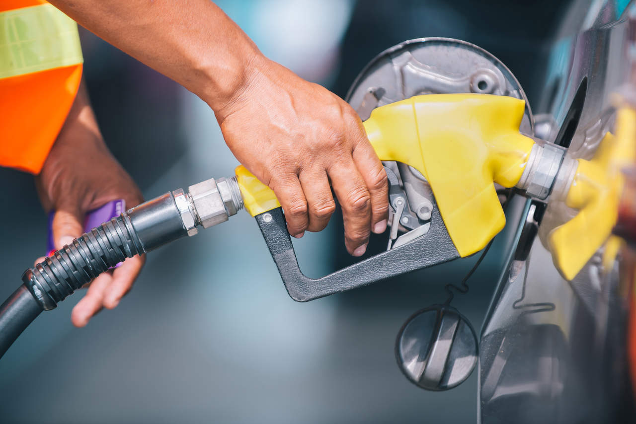 Mão de um frentista segurando a bico de uma bomba de combustível amarela enquanto abastece um carro, ilustrando o impacto do preço da gasolina no bolso do consumidor.