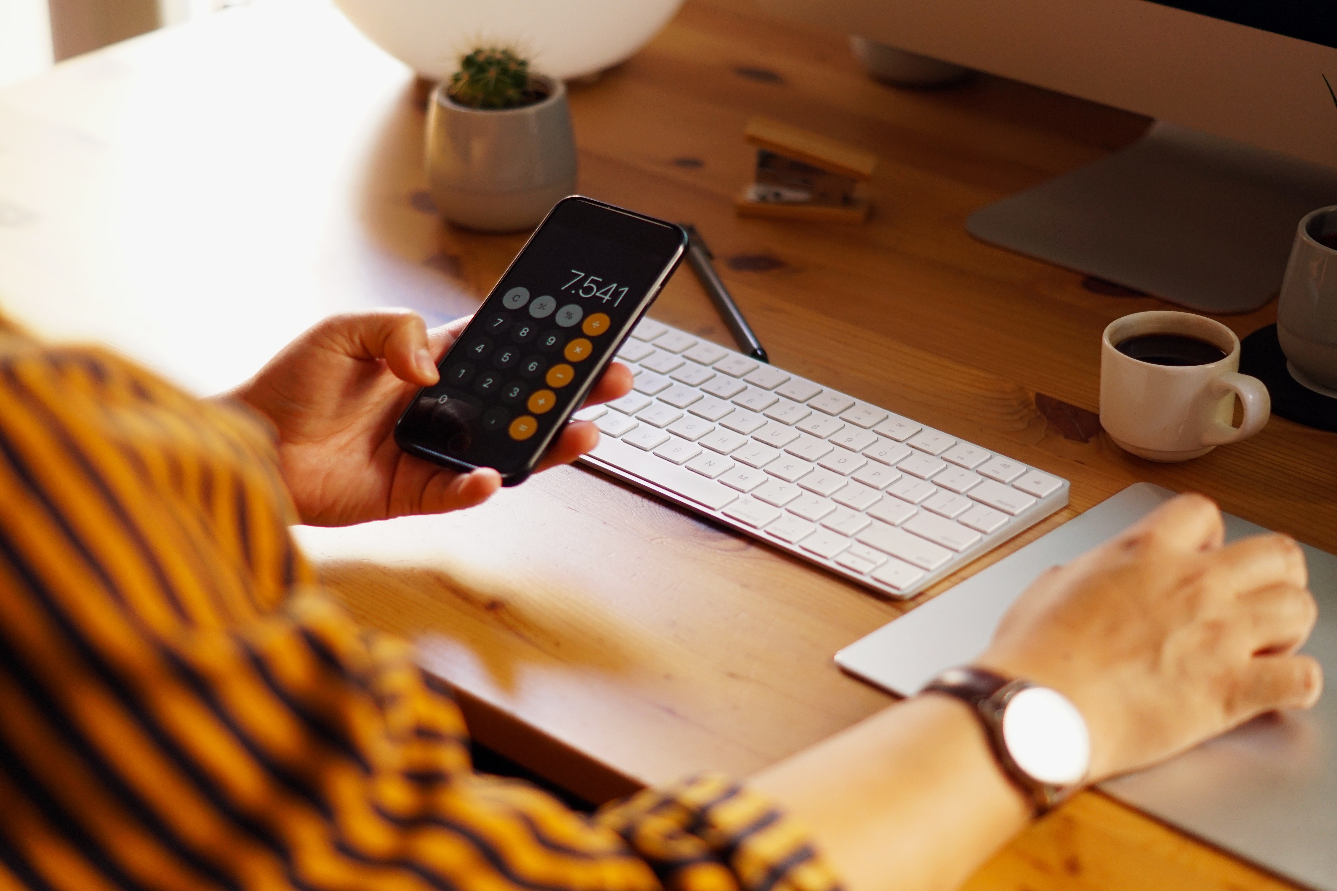 Pessoa analisando o caixa da empresa em uma mesa de escritório com o celular mostrando cálculos e um teclado ao lado.