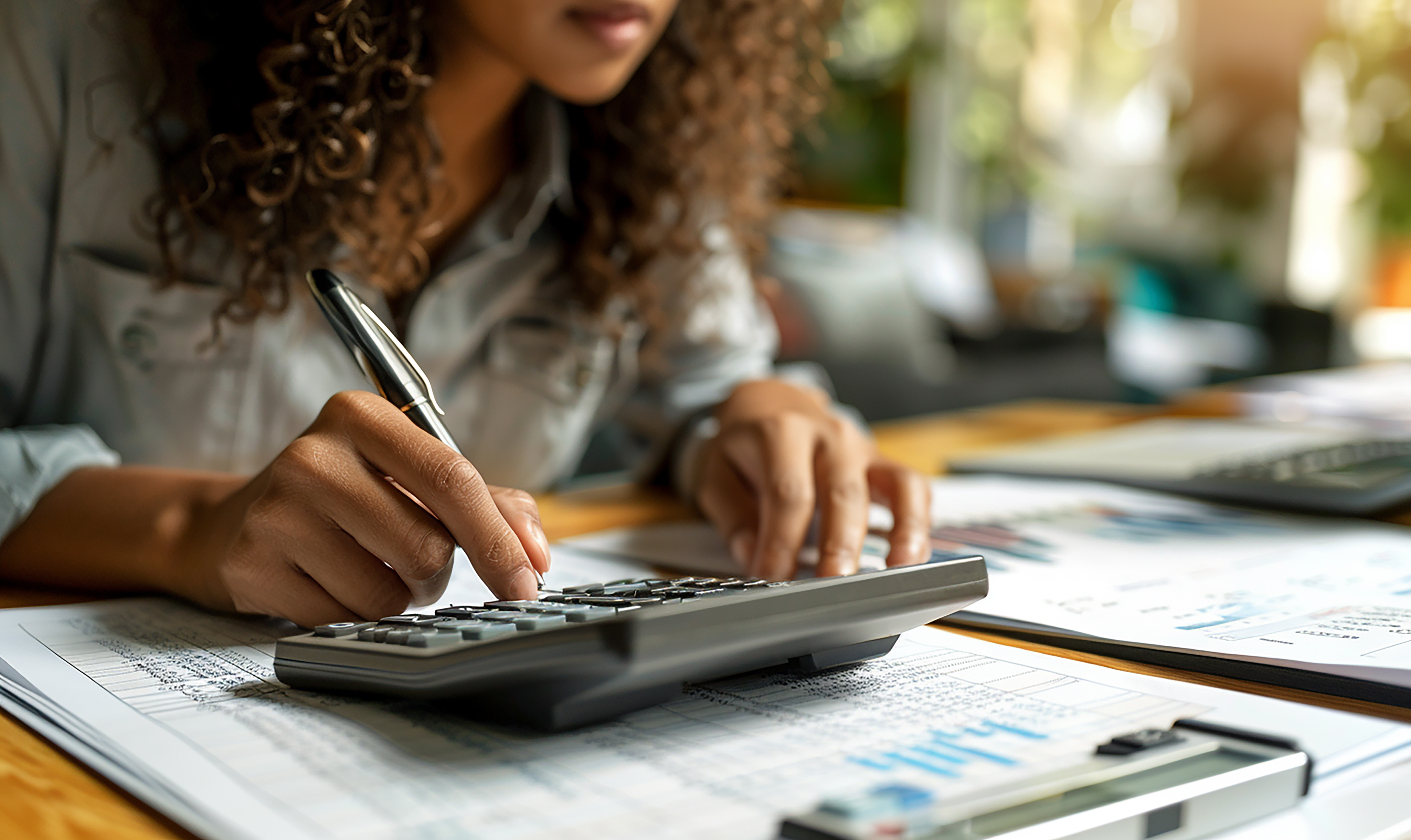 Mulher analisa demonstrativos financeiros e usa uma calculadora para avaliar o risco no caixa empresarial.