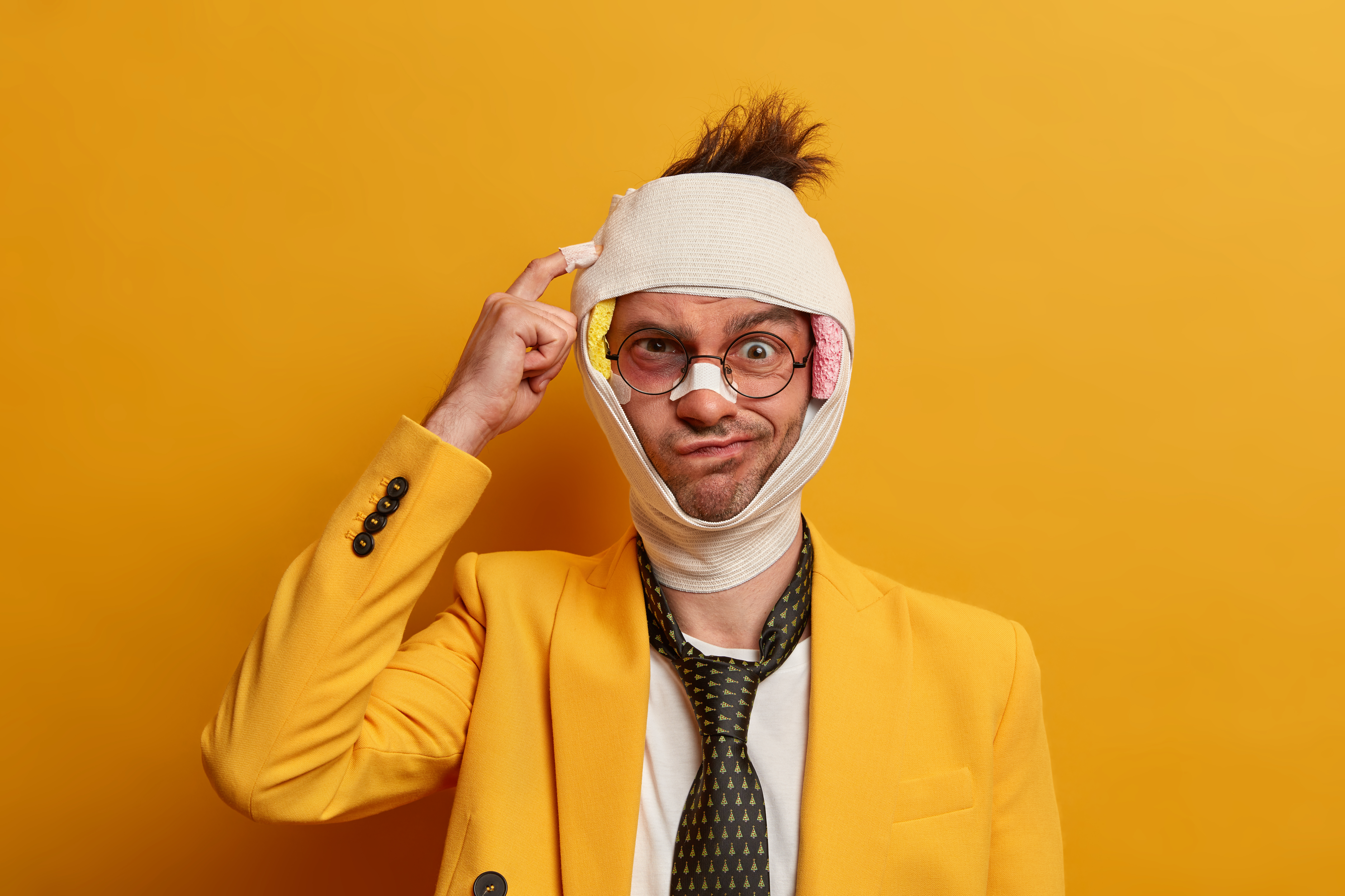 Homem de terno amarelo com a cabeça enfaixada e curativos no rosto, pensativo sobre quem paga o salário enquanto espera a perícia do INSS.