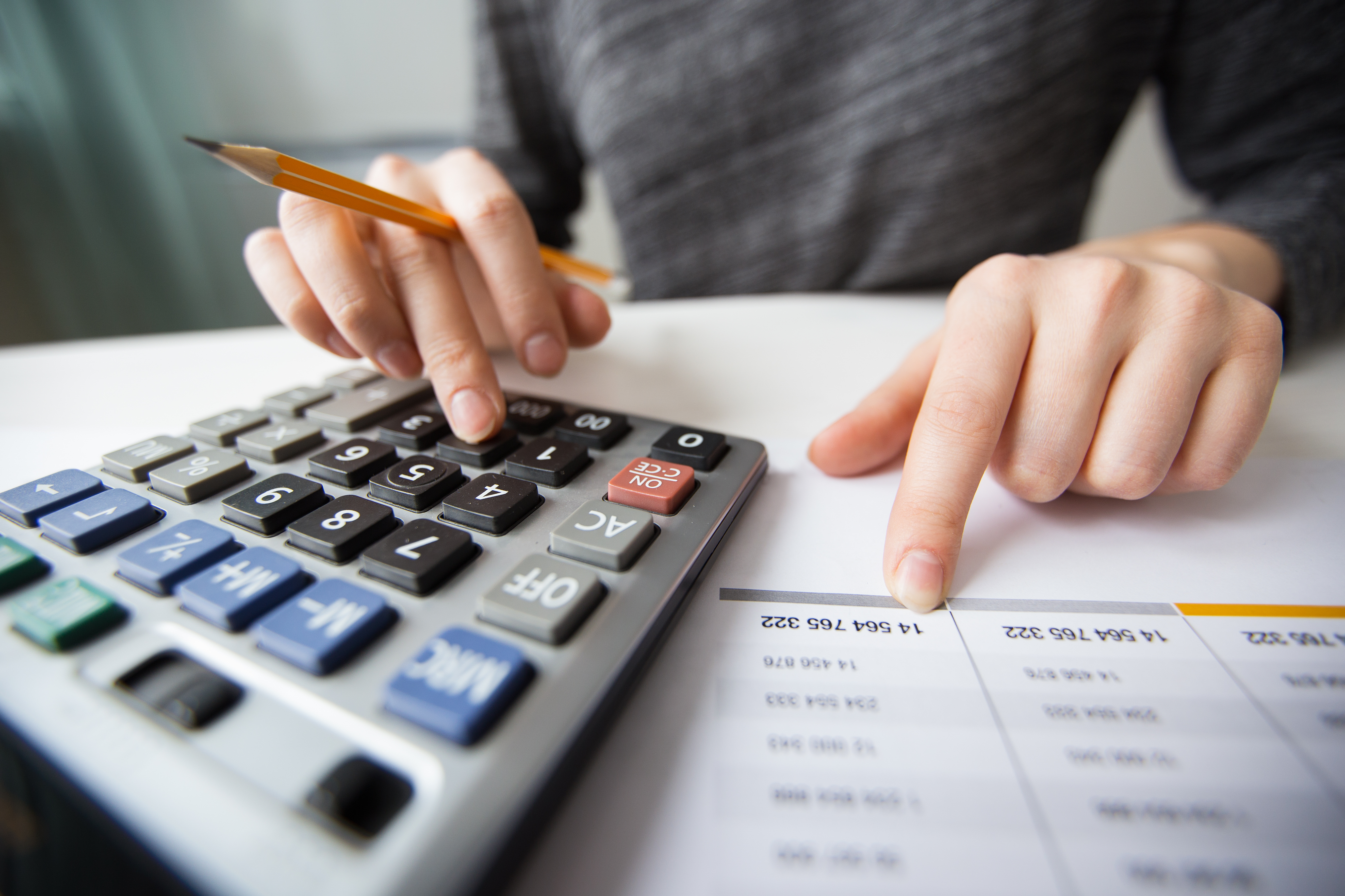Pessoa fazendo cálculos em uma calculadora sobre documentos para avaliar o impacto nas compras internacionais após o fim da taxa das blusinhas.
