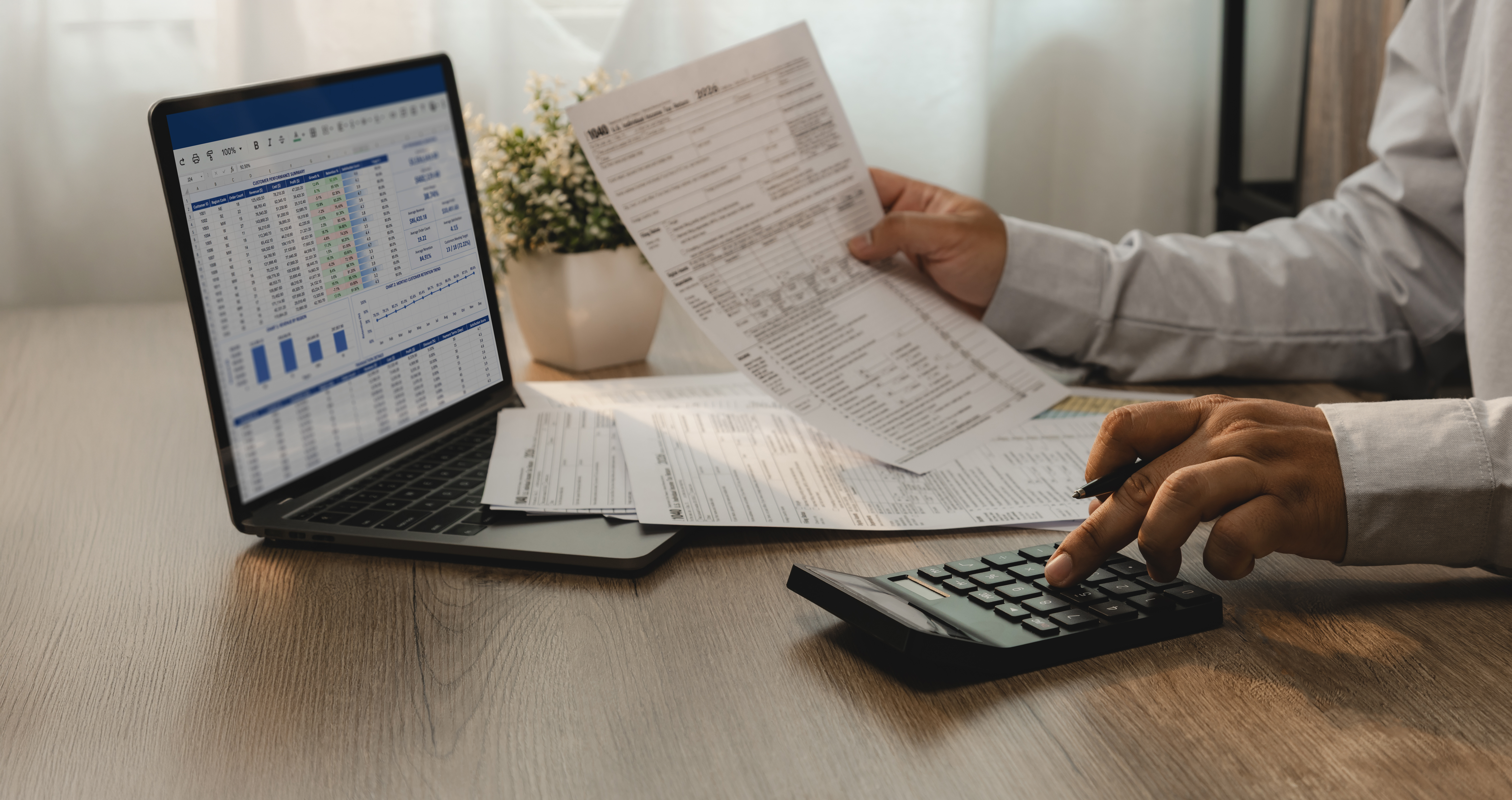 Profissional realiza gestão financeira rigorosa analisando planilhas no notebook, documentos e calculadora em uma mesa de madeira.